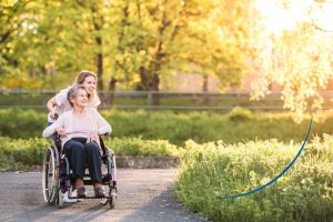 Frau im Rollstuhl wird von einer anderen Frau durch eine Grünanlage geschoben - Leistung Mobilität