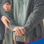 Nahaufnahme mit Fokus auf Hände. Junge Frau stützt eine Seniorin mit Gehstock