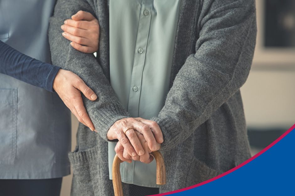 Nahaufnahme mit Fokus auf Hände. Junge Frau stützt eine Seniorin mit Gehstock